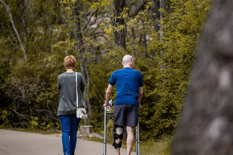Casal caminhando num parque, um deles em recuperação com apoio