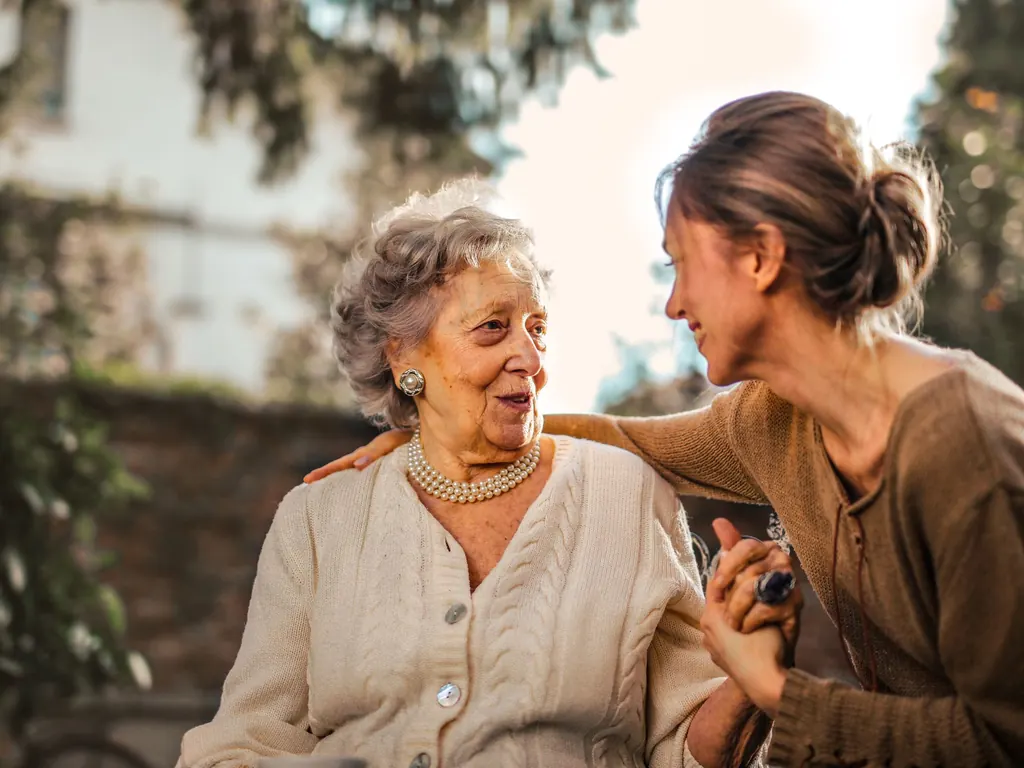 Filha sorrindo e conversando com a mãe idosa num jardim